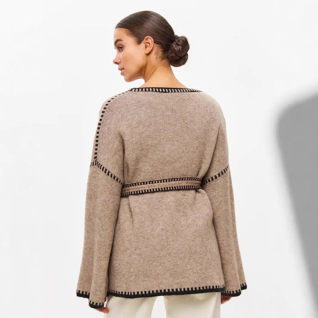 Loose beige knitted cardigan with a lace-up front, worn open over a white top.