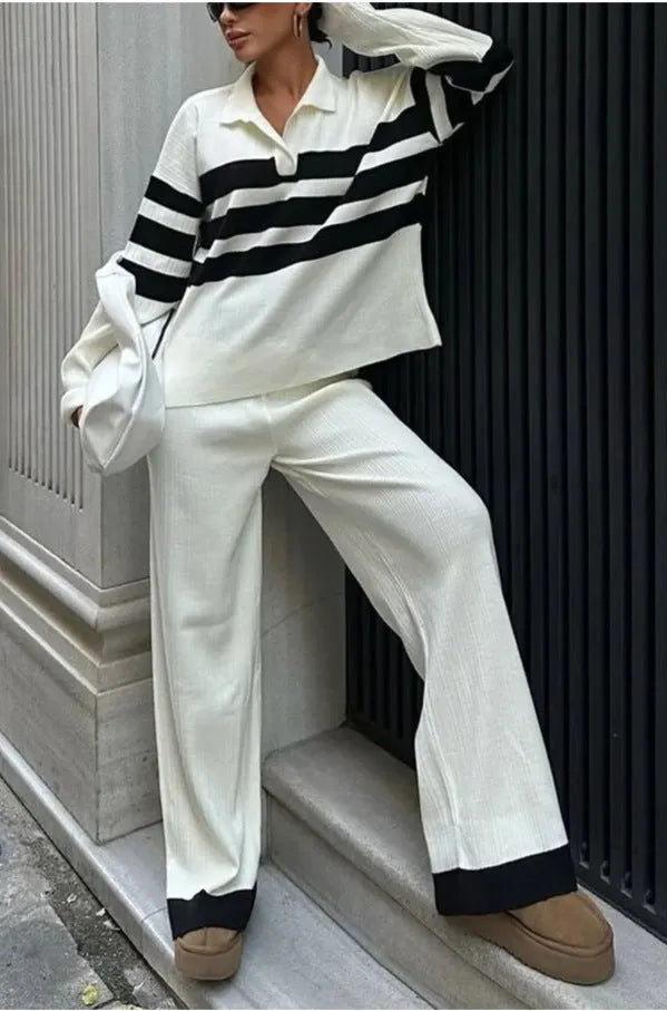 Women's black knitted polo shirt with white stripes and matching trousers laid flat.