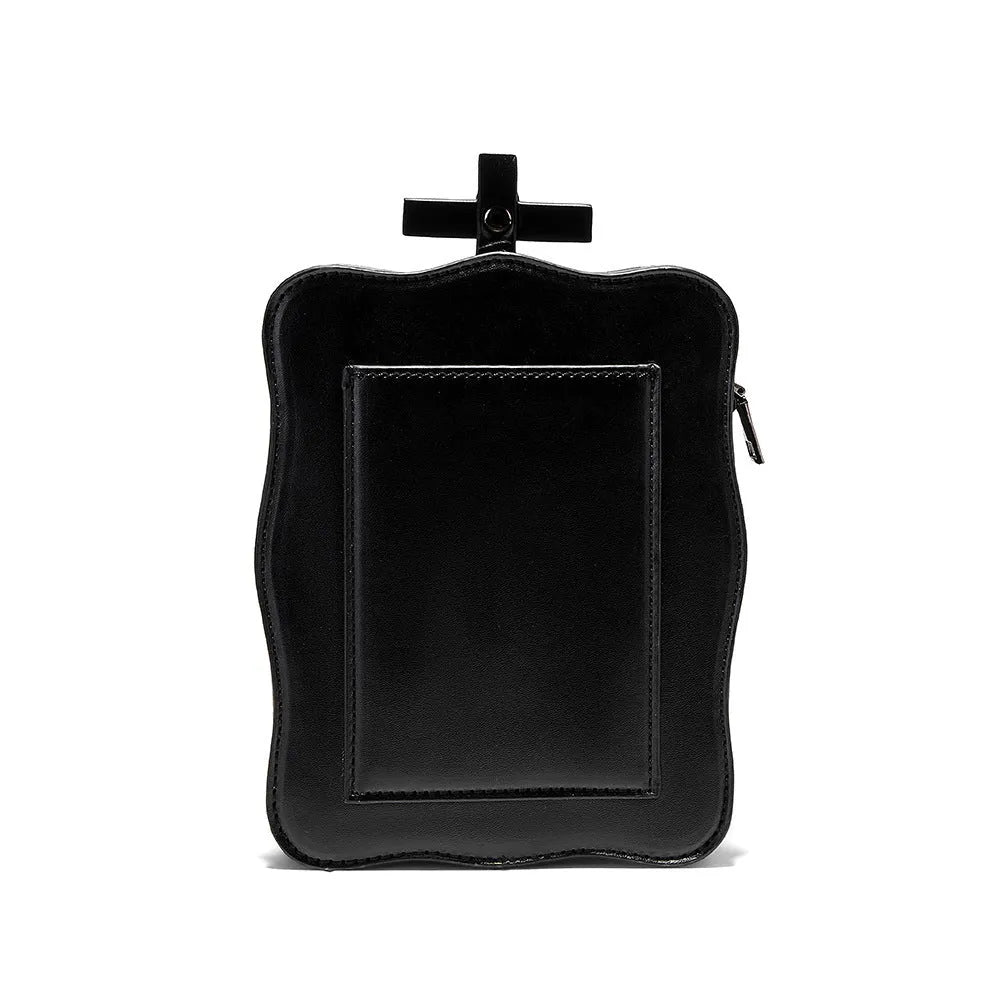 Black square crossbody bag with embossed skull design and metal chain strap against dark background