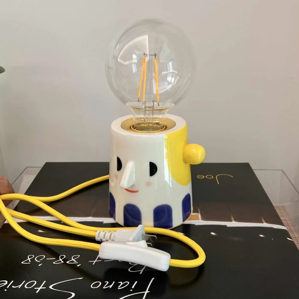 Handmade ceramic ball headlight lamp with a white glaze and integrated UK plug on a wooden table.