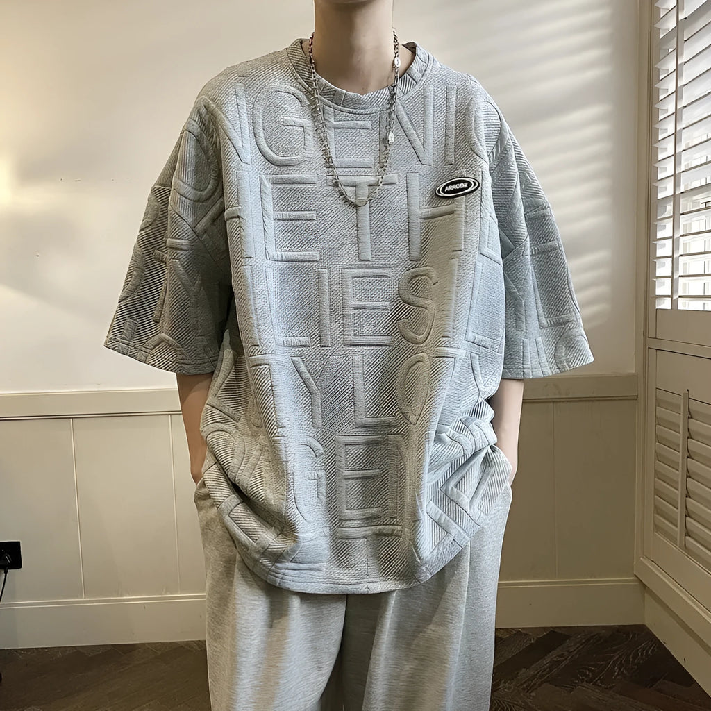Man modelling a grey loose-fit retro T-shirt with a raised 3D summer letter print on the front.