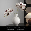 White ceramic ball vase with blue stripes, a silk blue orchid, on a wooden table.