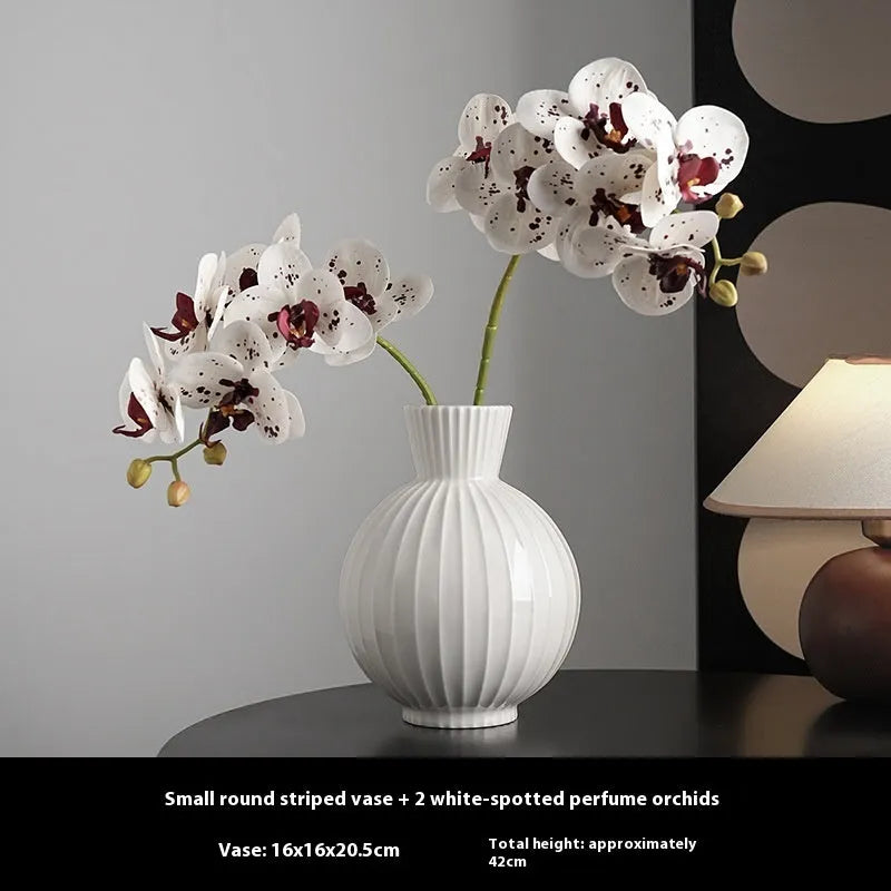 White ceramic ball vase with blue stripes, a silk blue orchid, on a wooden table.