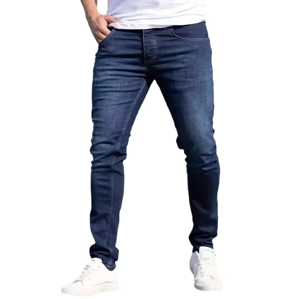 Men's dark blue slim-fit skinny jeans on a hanger, showing mid-waist and zipper fly detail.