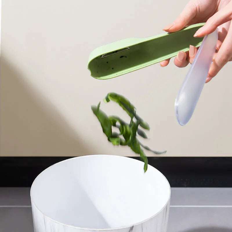 Dark green kitchen peeler with storage tube and stainless steel blade on a worktop.