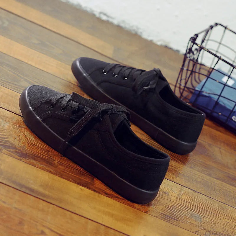 All black women's low-top canvas flat shoes with flat rubber sole and lace-up front.