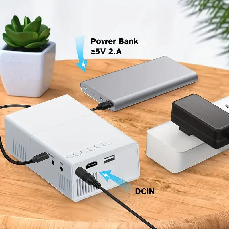 Black and white M100 mini portable LED home projector with remote control on a table.