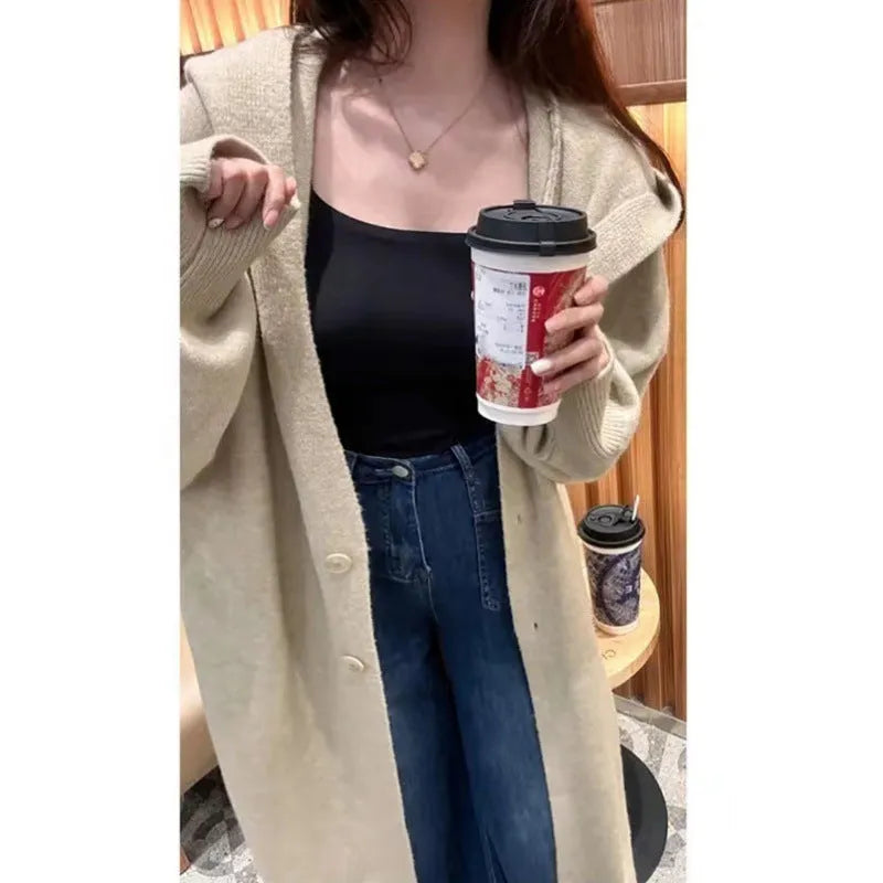 A woman wearing a long, loose, beige hooded knitted cardigan in a Korean casual style.