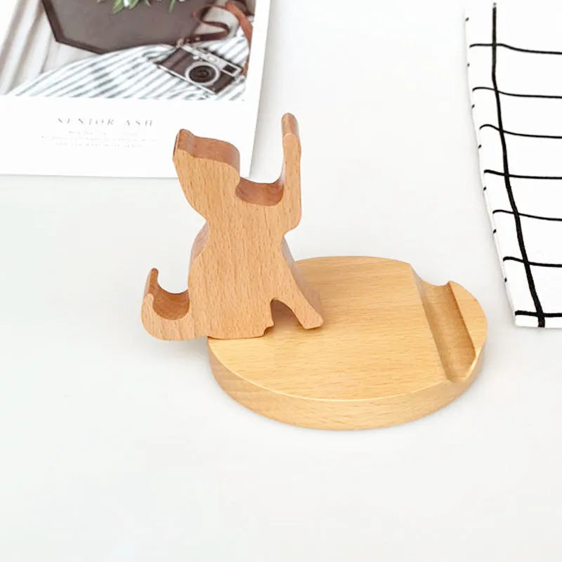 Solid beech wood phone stand with a decorative resin puppy figurine, holding a mobile phone at an angle with a charging cable threaded through the back.