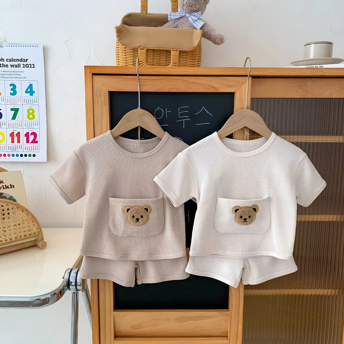 Unisex baby summer suit with bear print cotton top and beige shorts on a neutral background