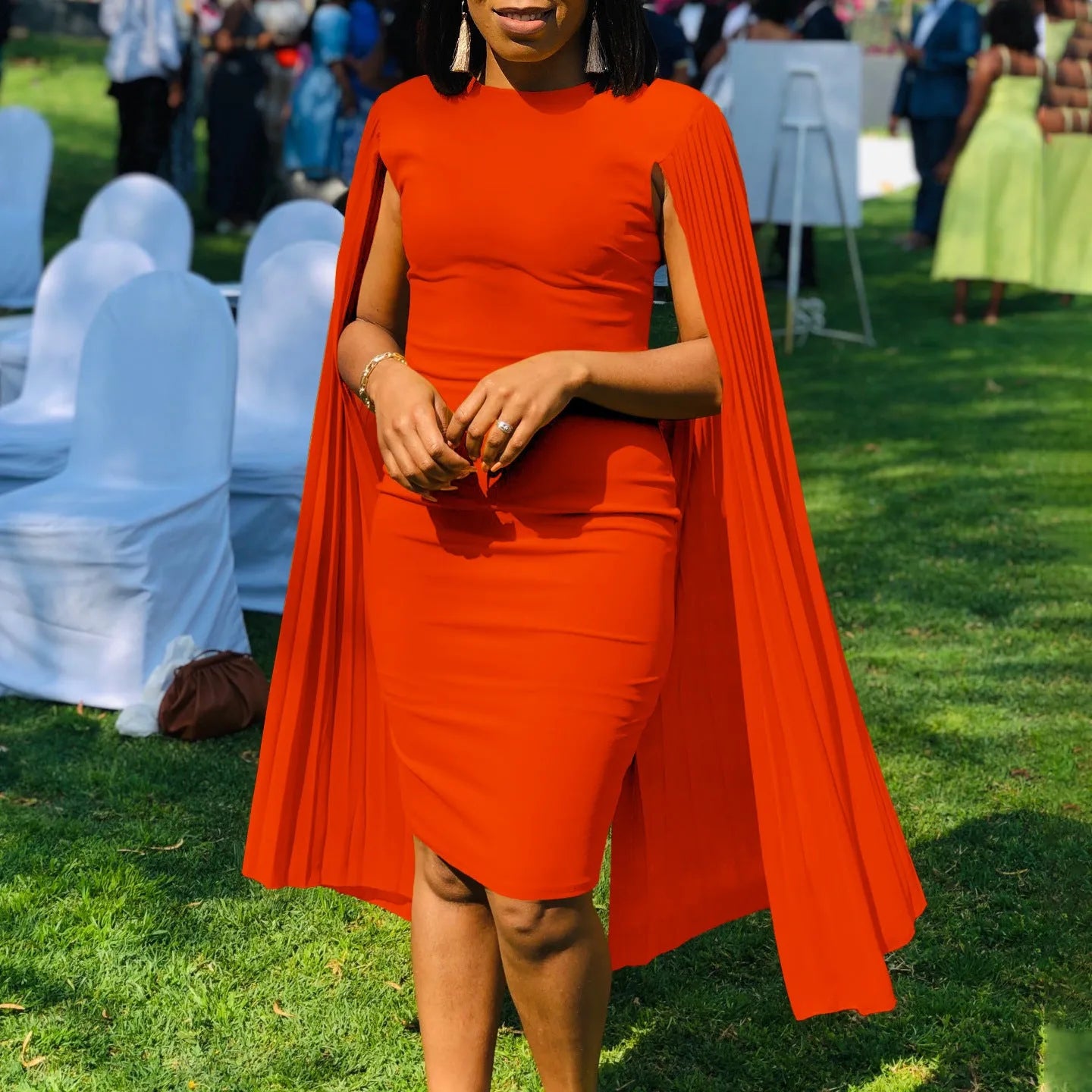 A woman wearing a long sleeve, high-waist pleated evening gown in a solid colour, showcasing the floor-length skirt and round neckline.