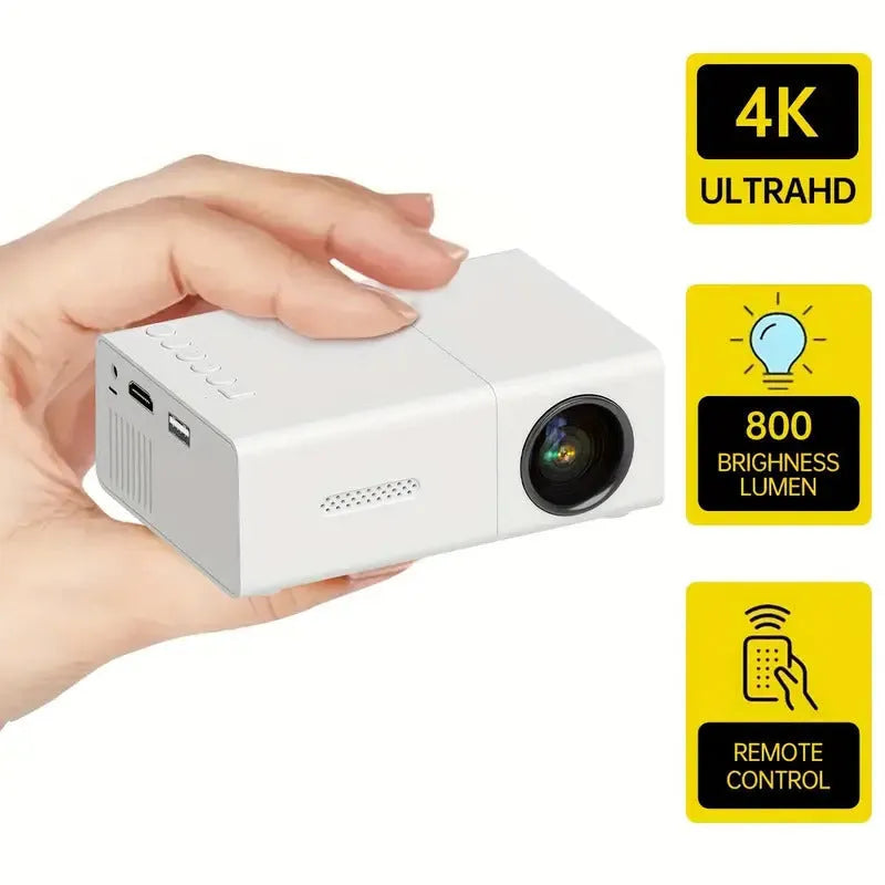 Black and white M100 mini portable LED home projector with remote control on a table.