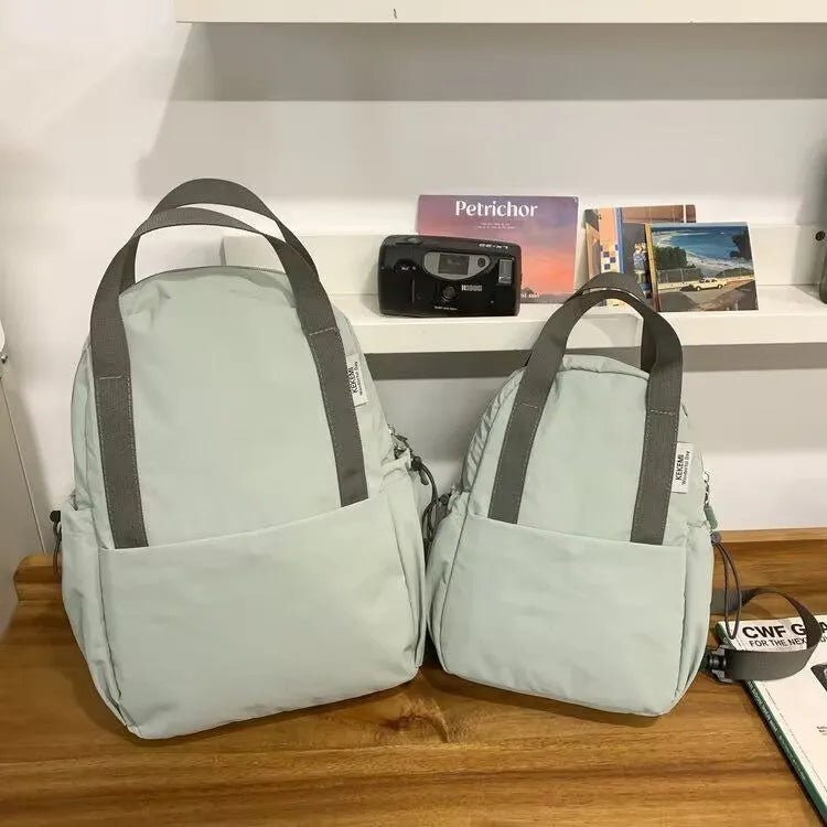 Simple solid colour nylon backpack in black on a neutral background, showing curved shoulder straps and top lock.