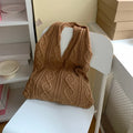 Women's white hollow knitted crochet tote bag with double shoulder straps, shown on a table.