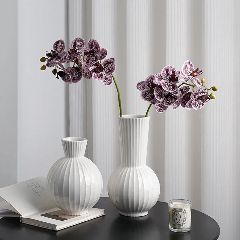 White ceramic ball vase with blue stripes, a silk blue orchid, on a wooden table.