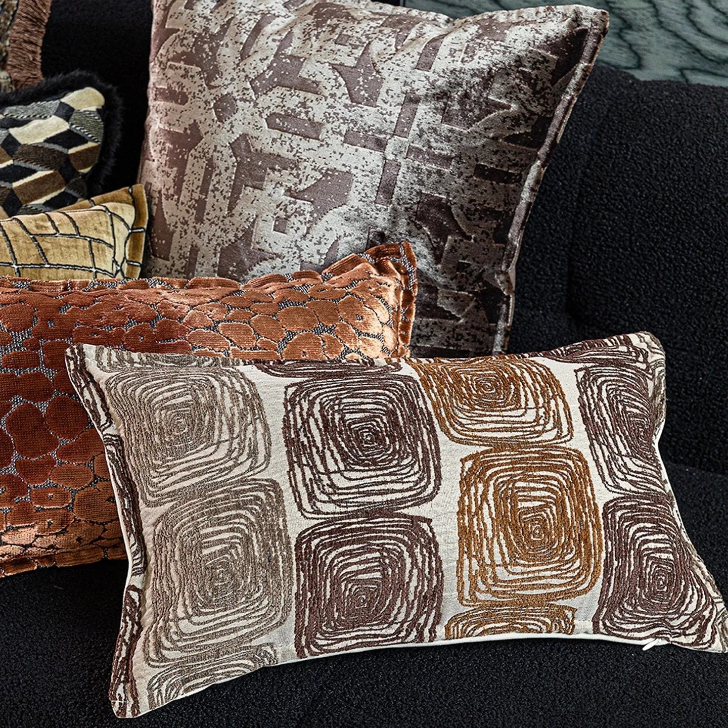 Cream and coffee coloured abstract coil pattern square and waist pillow covers on a sofa.