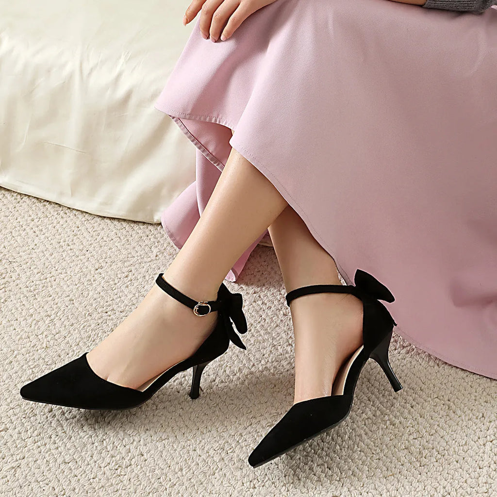 Women's black suede stiletto high heels with pointed toe and decorative bowknot.