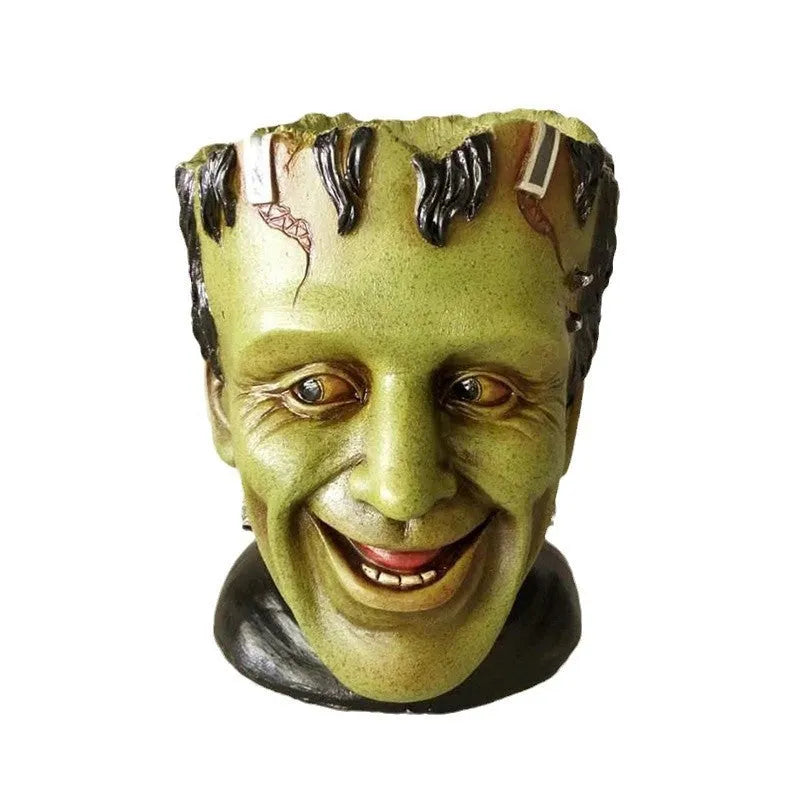 Green Frankenstein monster resin flower pot on a desk with a small succulent plant inside