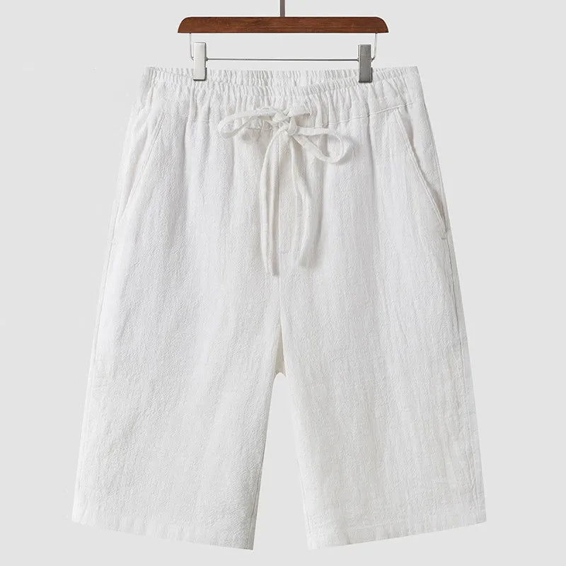 Pair of beige men's casual linen shorts with a loose fit and cropped length on a plain background.