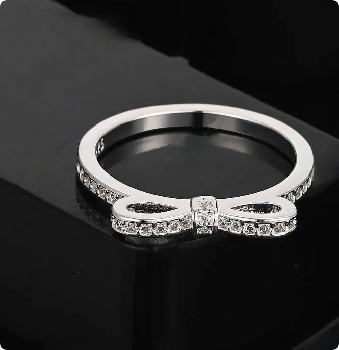 Silver coloured ring with a detailed three-dimensional bow design set with sparkling zircon crystals on a finger.