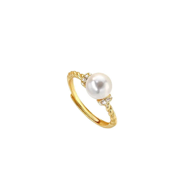 Close-up photo of an antique-style twisted copper ring with a small white pearl inlaid on a person's finger.