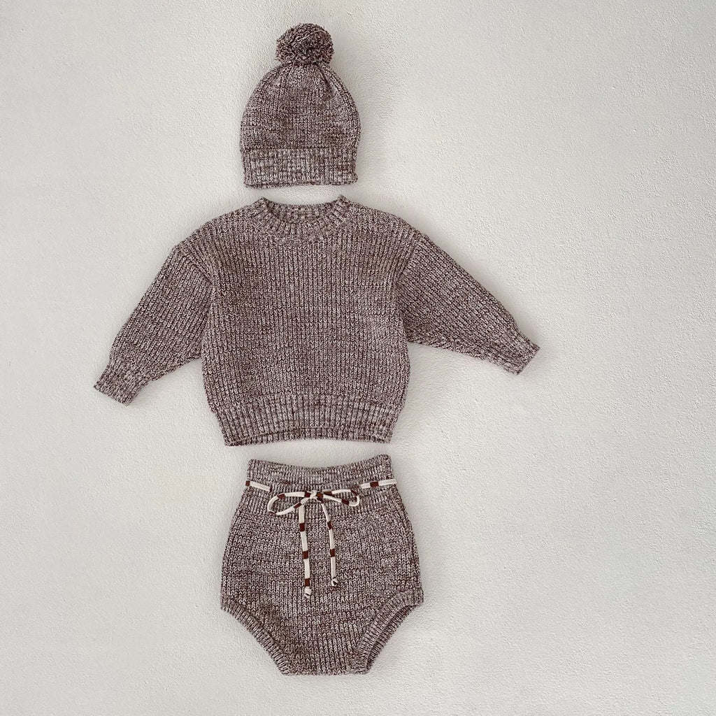 Dark brown knitted three-piece set for infant girl with fur ball hat, blouse, and shorts.