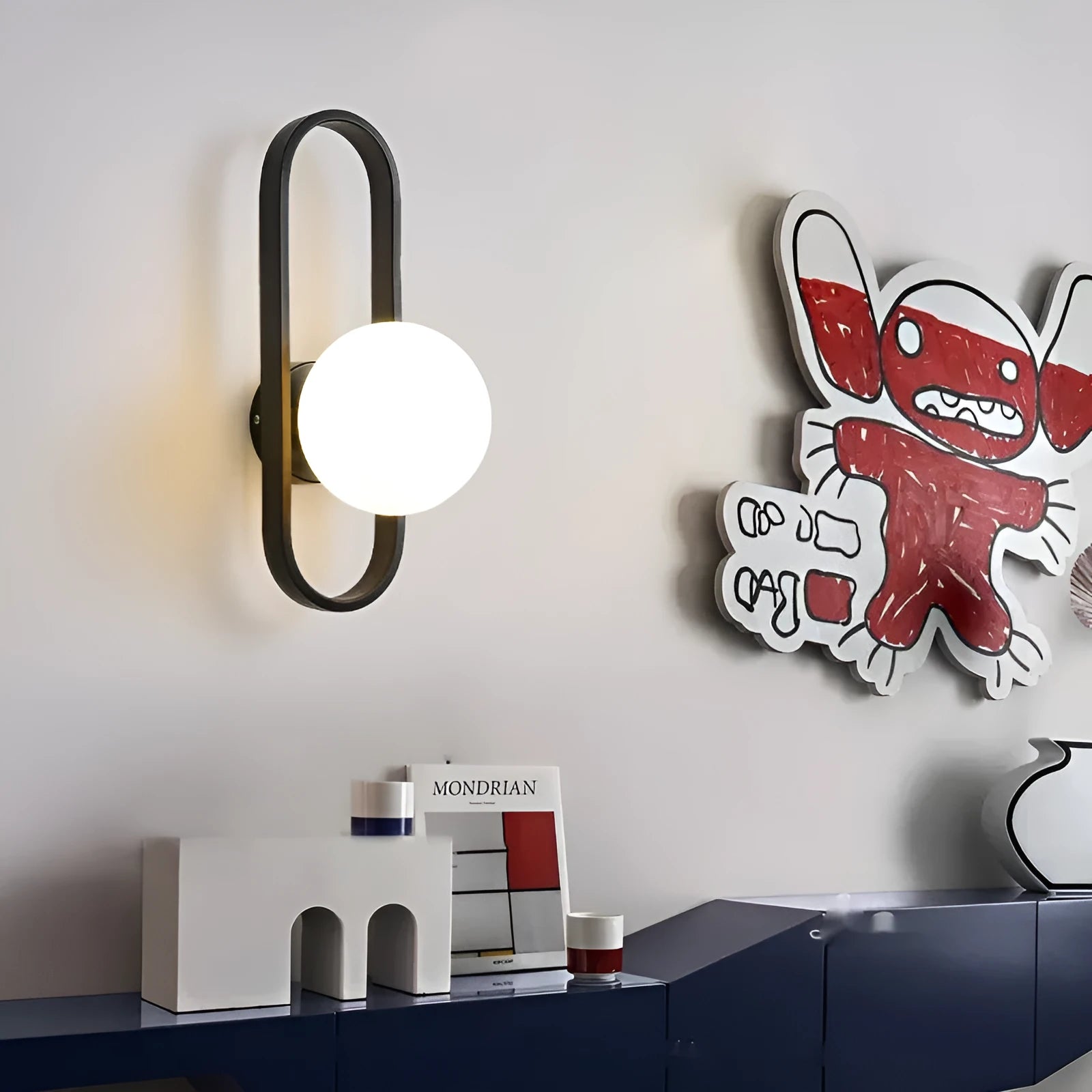 Minimalist wall-mounted lamp with clear glass bulb shade on a black iron sconce arm and backplate.