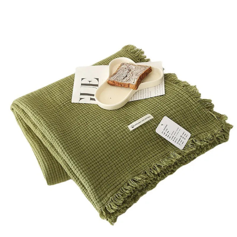 Cotton four-layer gauze blanket with tassel trim in avocado green colour, laid flat.