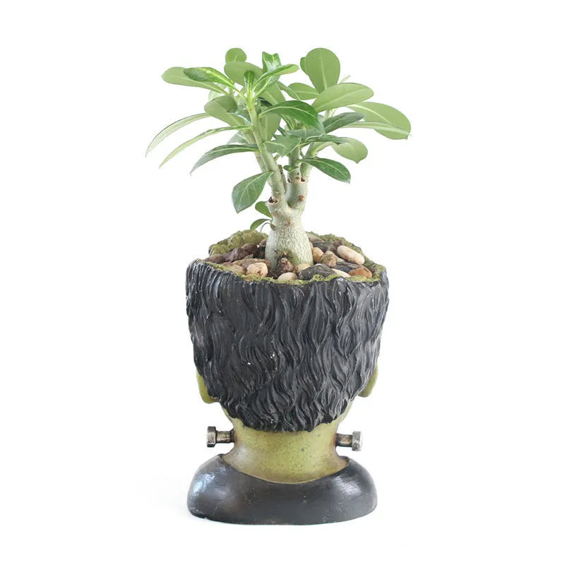 Green Frankenstein monster resin flower pot on a desk with a small succulent plant inside