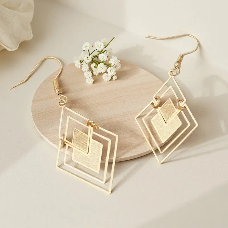 Gold rhombus hollow stud earrings with diamond shape on a light background