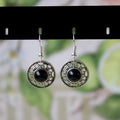 A pair of handmade ethnic earrings with a silver flower disc design, turquoise stones, and red decorative accents.