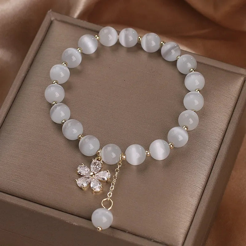 Women's white cat's eye stone bracelet with floral detail and a safety buckle pendant on a single loop.