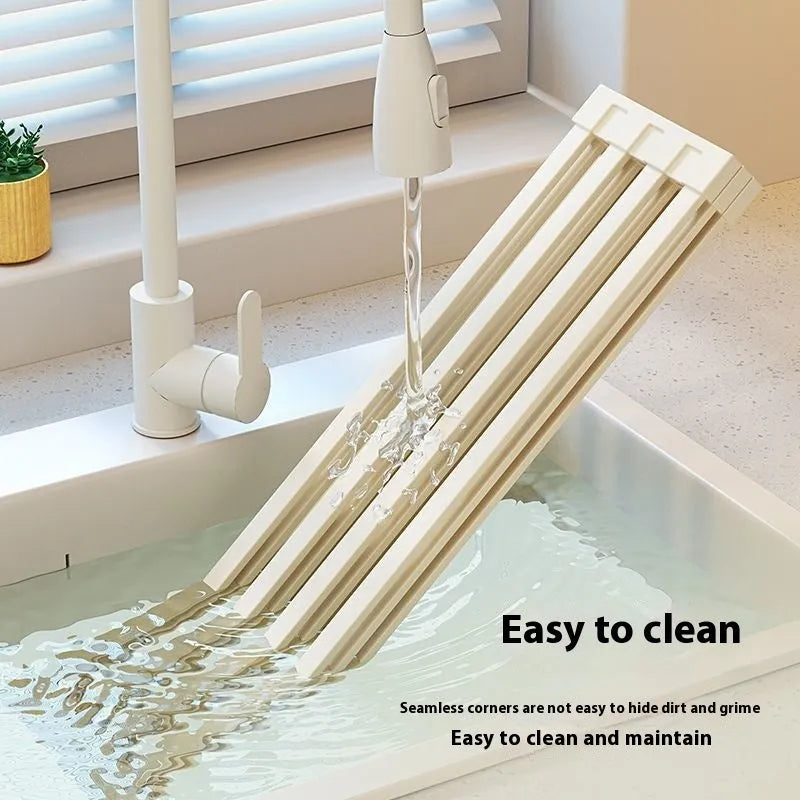 Milky White foldable stainless steel kitchen draining rack shown beside a sink, demonstrating its tri-fold mechanism.
