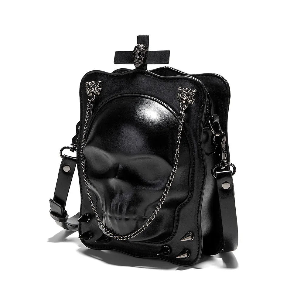 Black square crossbody bag with embossed skull design and metal chain strap against dark background