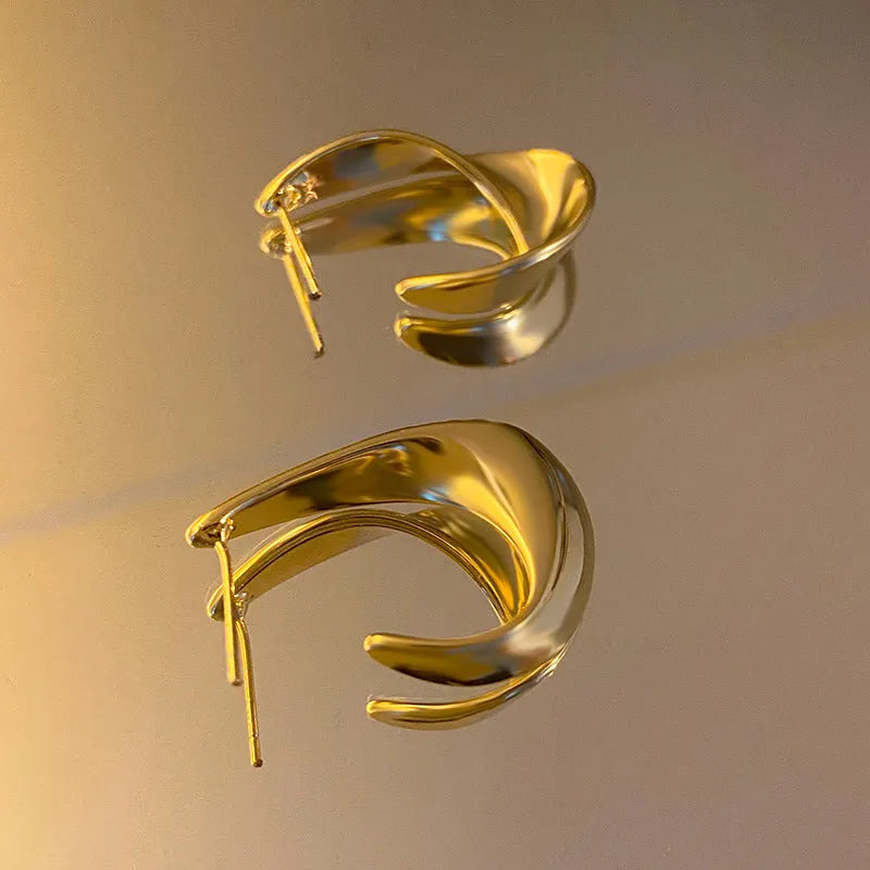 A pair of twisted geometric round metal earrings with a gold electroplated finish on a white background.