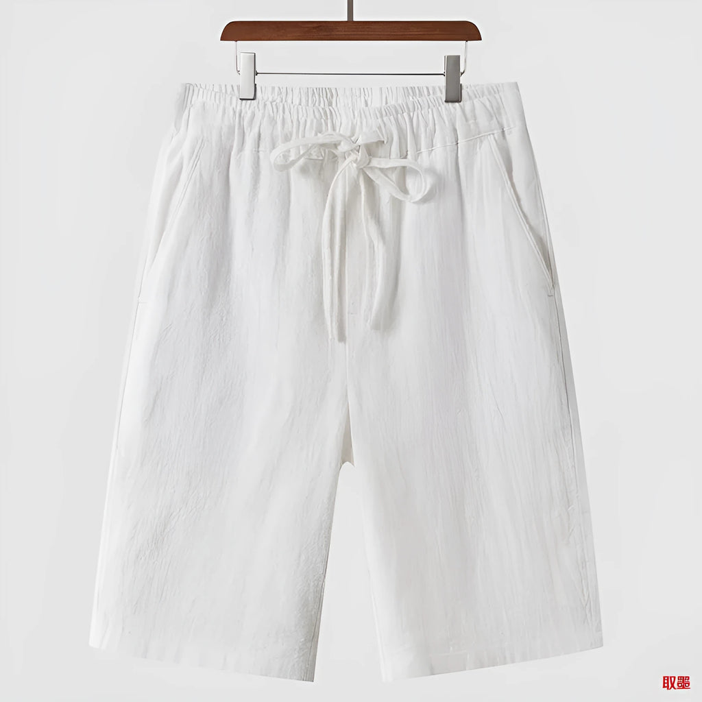 Pair of beige men's casual linen shorts with a loose fit and cropped length on a plain background.