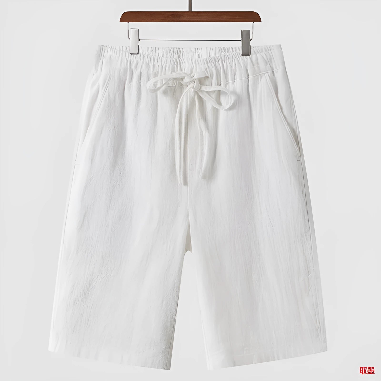 Pair of beige men's casual linen shorts with a loose fit and cropped length on a plain background.