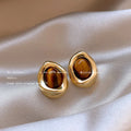 Handmade geometric alloy earring set showing three styles: round pieces, amber studs, and tigereye drops with tassels.