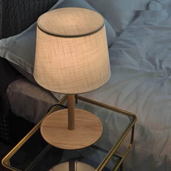 Walnut coloured solid wood bedside lamp with a white cloth lampshade and a black cable switch.
