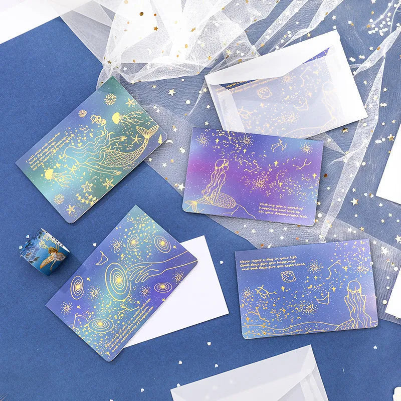 Set of three bronzing mermaid-style folded greeting card envelopes in celestial colourways, 13x8.5cm, on a light background