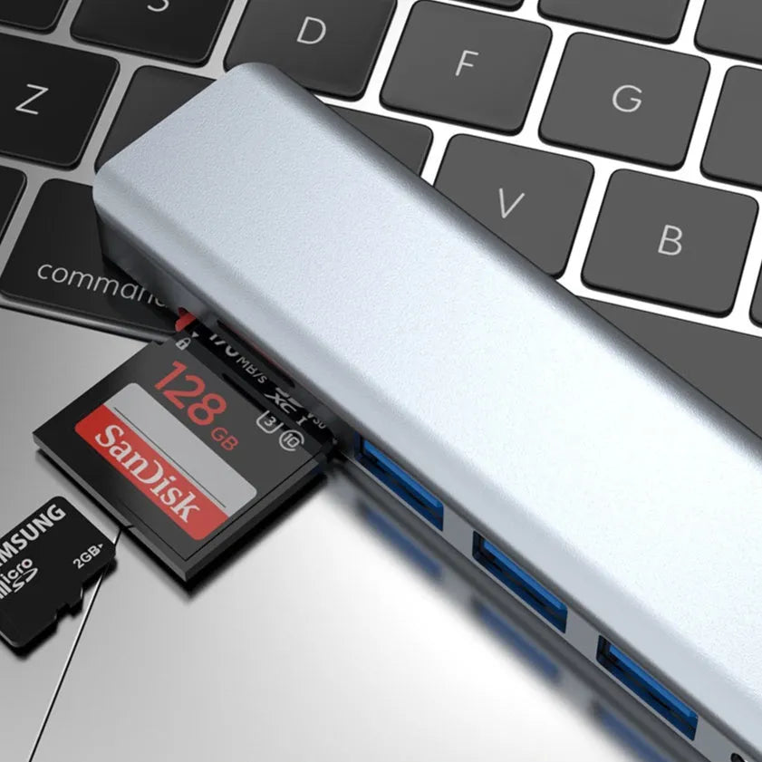 Silver 7-in-1 USB C hub docking station with HDMI, USB ports, and card readers on a desk.