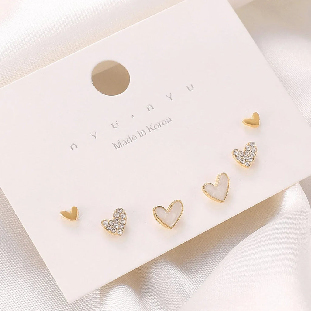 Set of three pairs of women's heart-shaped alloy earrings in gold, black, white, and pink.
