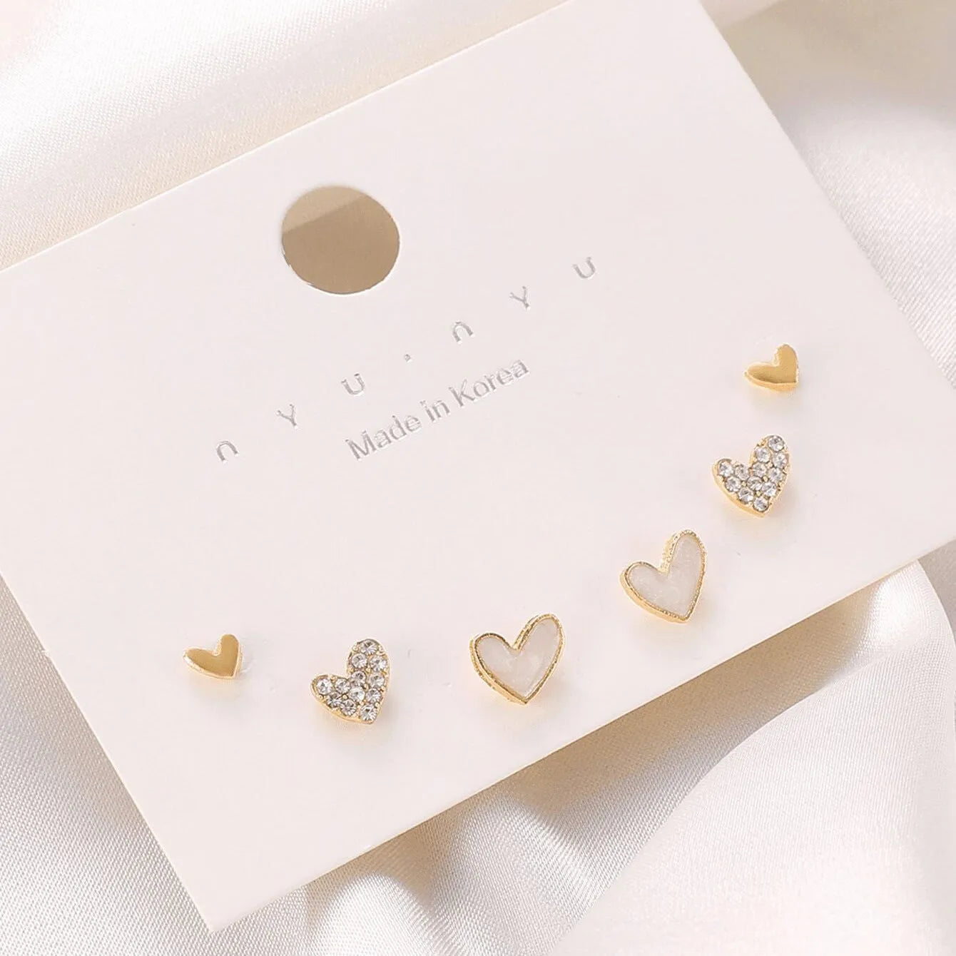 Set of three pairs of women's heart-shaped alloy earrings in gold, black, white, and pink.