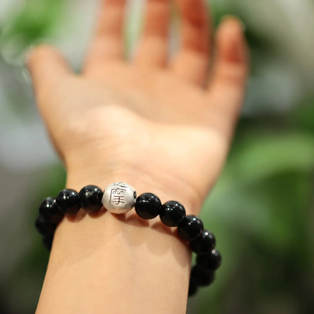 Close-up of a black bracelet with 10mm agate beads and sterling silver details on a wrist.