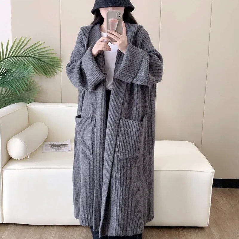 A woman wearing a long, loose, hooded cardigan coat in a neutral colour, showing its oversized fit and length.