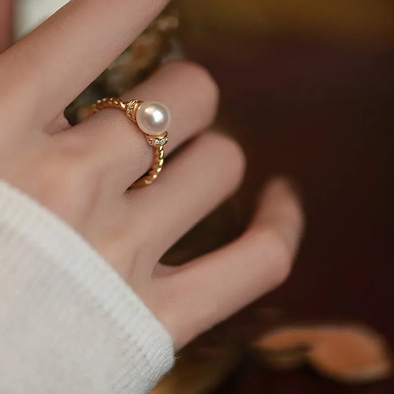 Close-up photo of an antique-style twisted copper ring with a small white pearl inlaid on a person's finger.