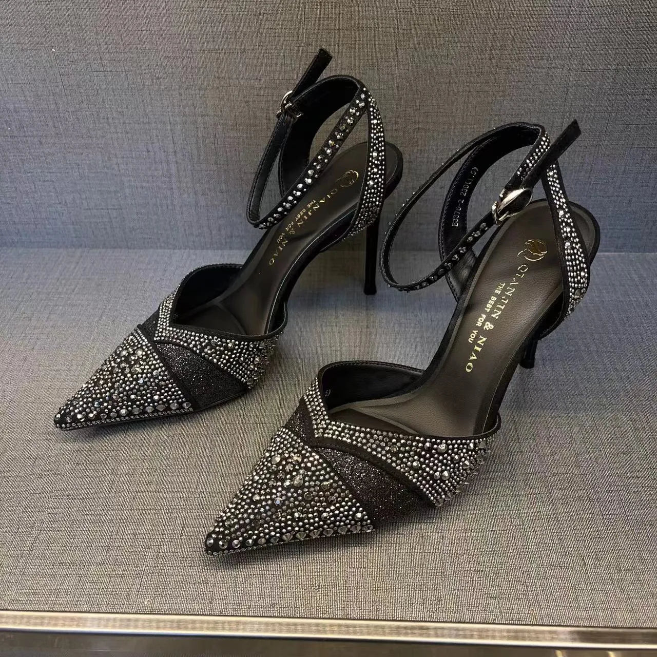 Women's black hollow high heel shoe with red sole and pointed toe, shown next to a silver pair.