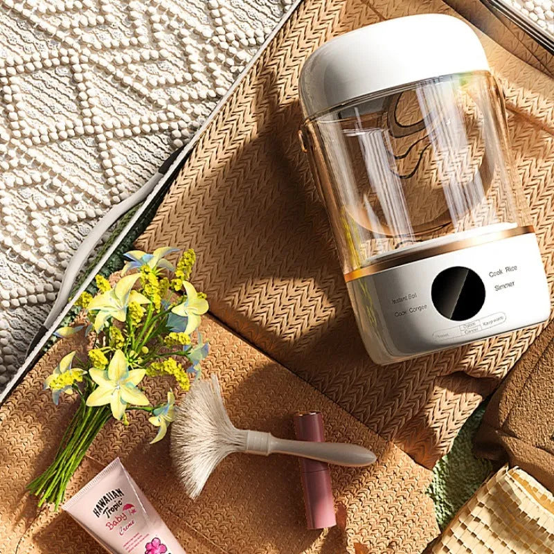 Personal portable electric stew cooker with transparent glass pot and fibreglass body on a desk.