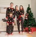 Family wearing matching red plaid Christmas pajamas, including parents, two children, a baby, and a dog.