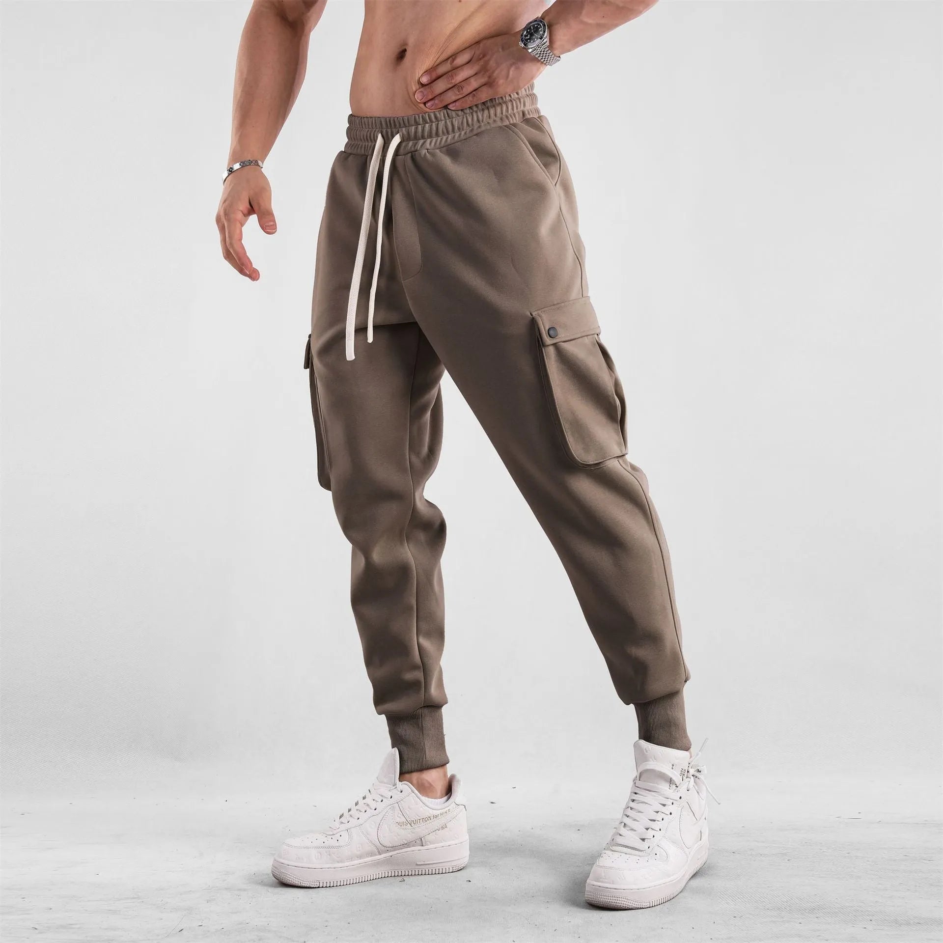 Men's loose-fit beige trousers with ankle ties and multiple pockets, laid flat.